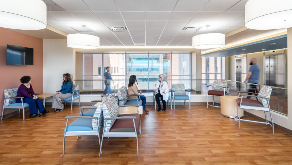 Presbyterian Hospital new patient tower waiting area with people on chairs, with view of bridge through glass wall